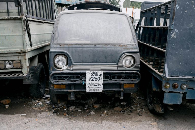A close-up of a weathered truck with a faded license plate parked on a Faisalabad street.